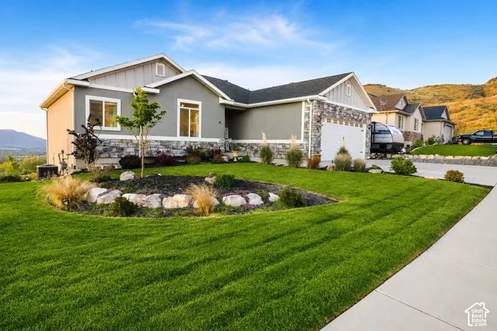 Single-story exterior featuring a stone and siding facade, a three-car garage, and landscaped front yard with stone-lined garden beds