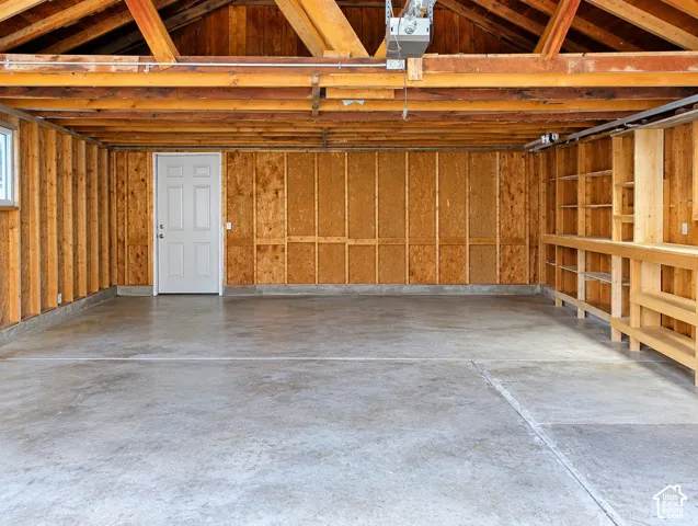Garage space featuring exposed timber framing, concrete flooring, built-in wooden shelving, and a six-panel door