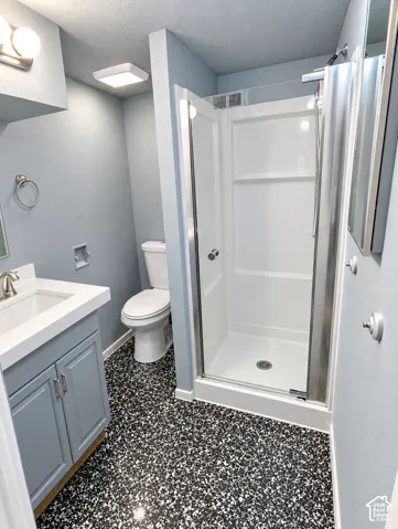 Bathroom featuring a vanity with a solid-surface countertop, walk-in shower with a glass enclosure, and patterned high-contrast flooring