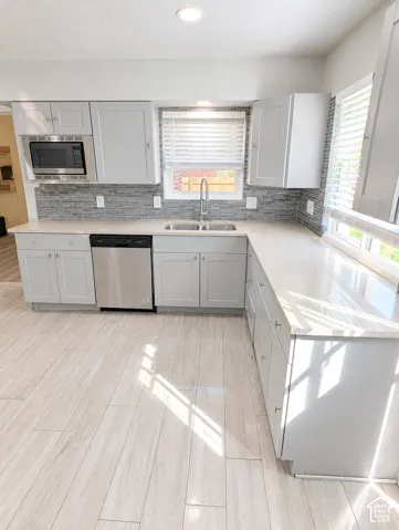 Kitchen featuring light-gray shaker cabinetry, stone-finish countertops, stacked-tile backsplash, stainless steel dishwasher, and wood-finish flooring