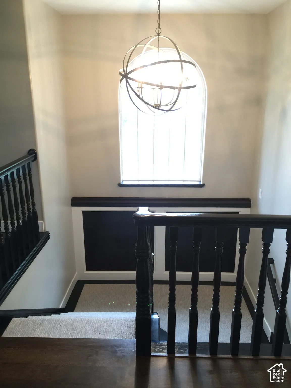 Arched window, orb-style metal chandelier, dark wood-finish staircase railing with turned balusters, and wainscoting detail