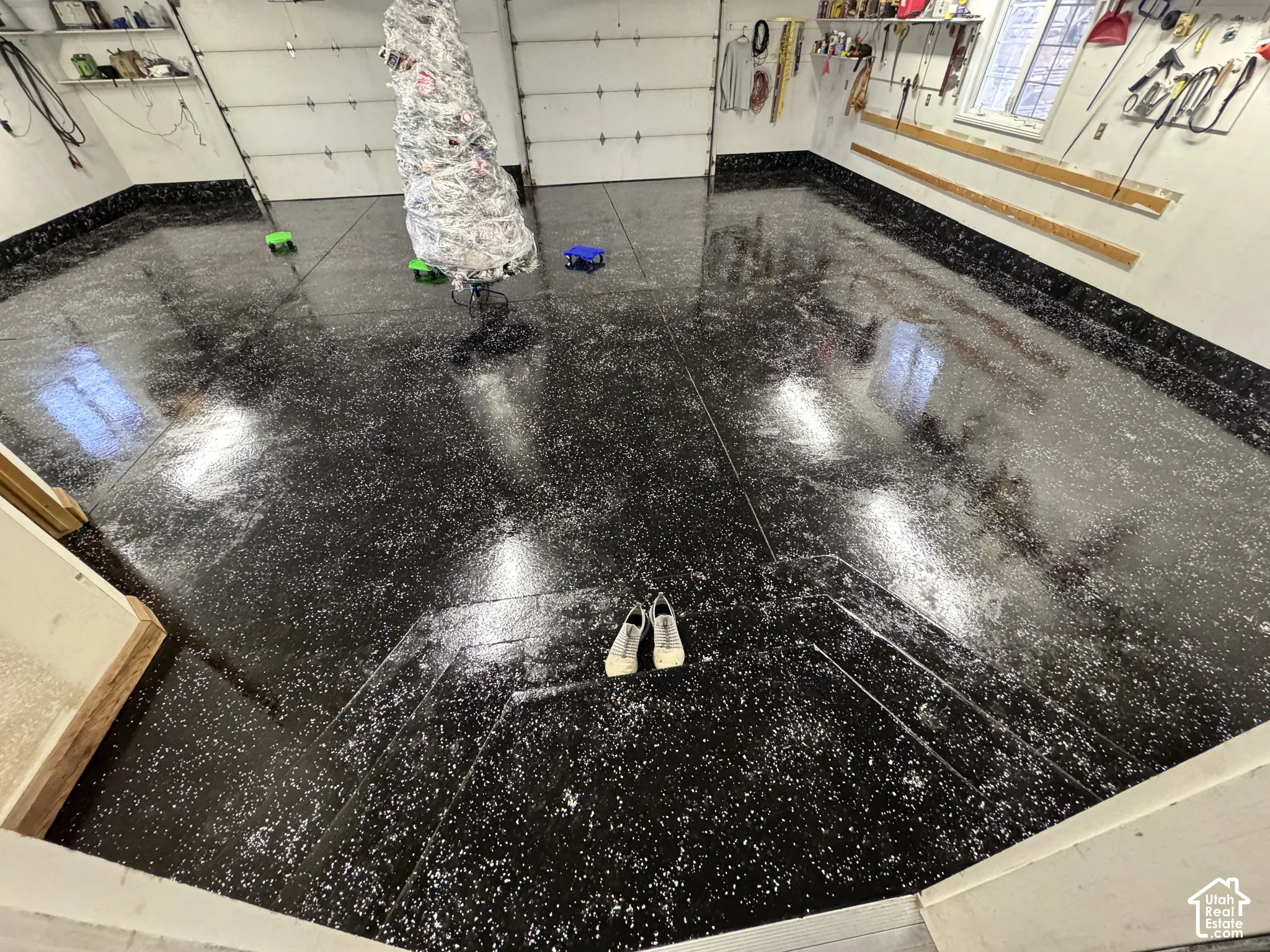 Garage featuring a high-gloss speckled epoxy floor coating, integrated wall-mounted storage tracks, and two overhead garage doors