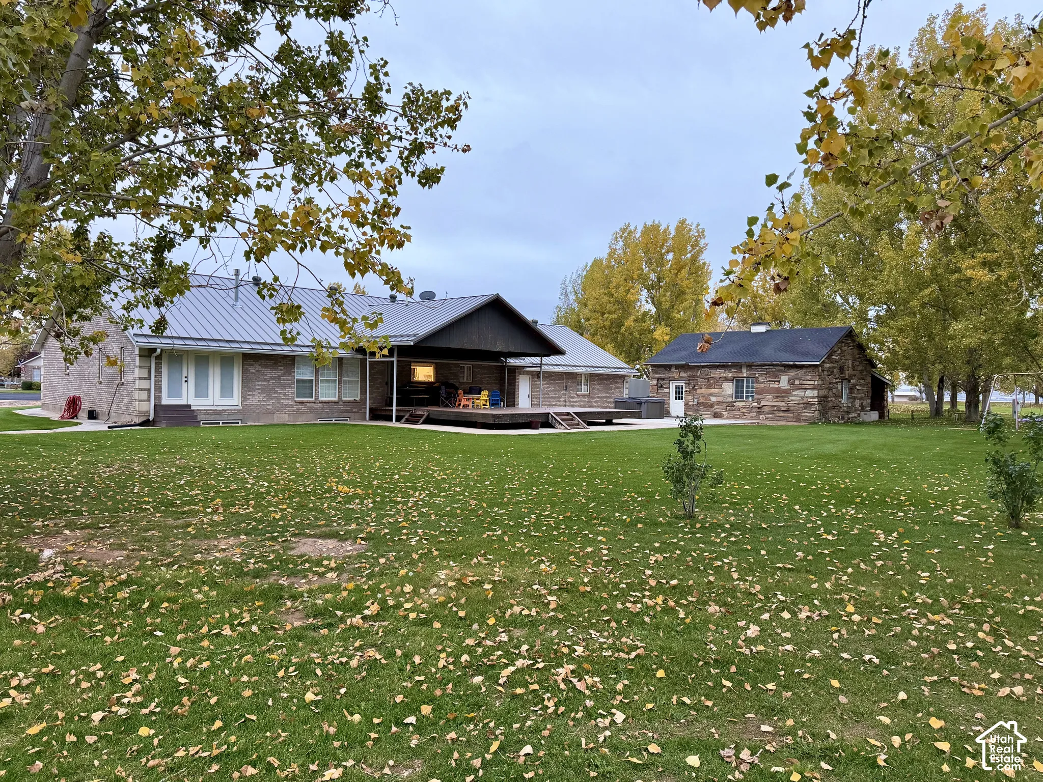 Expansive backyard featuring a brick exterior, standing-seam metal roof, covered patio, and detached stone-clad outbuilding