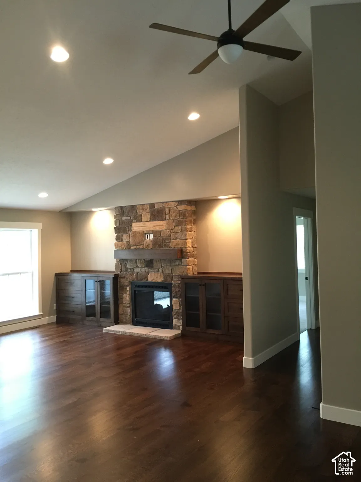 Vaulted ceilings featuring a ceiling fan, wood-finish flooring, and a stone-clad fireplace with built-in dark wood cabinetry