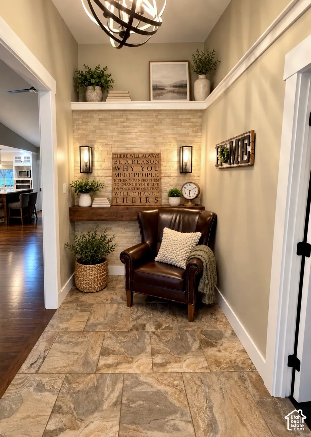 Foyer featuring large-format stone tile flooring, stacked stone wall accent, integrated floating wood mantel, wall-mounted sconces, and a decorative spherical chandelier