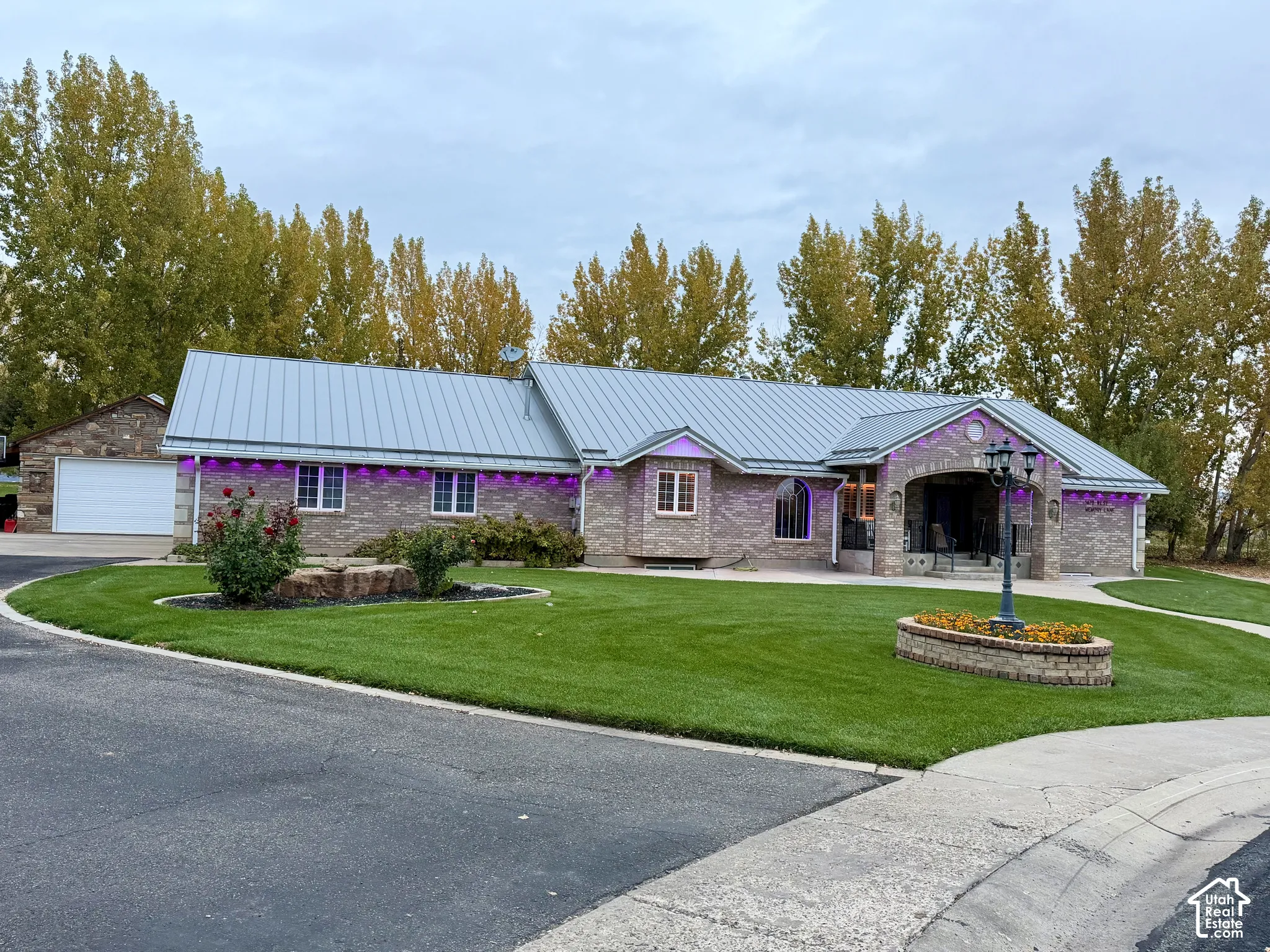 Single-story brick exterior featuring a metal roof, arched covered entryway, manicured lawn, and detached garage