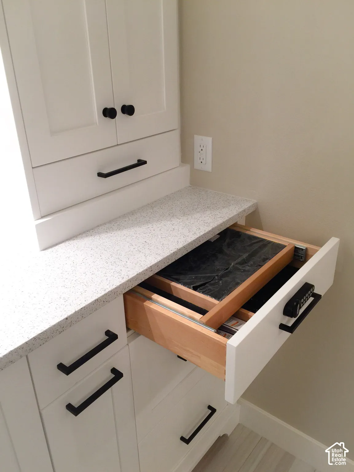 Built-in white cabinetry featuring matte black hardware, speckled composite countertop, and a drawer equipped with an integrated electronic keypad lock