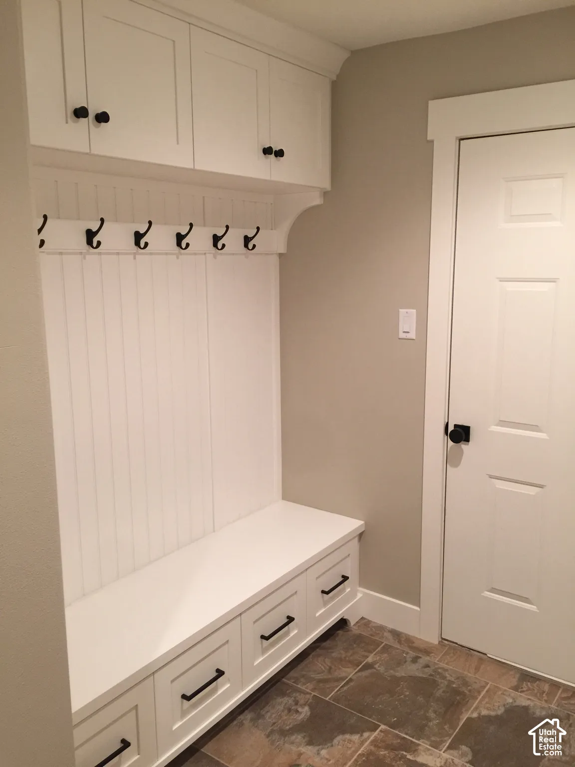 Built-in cabinetry with beadboard detailing, upper storage lockers, lower drawers, matte black hardware, and slate-finish tile flooring