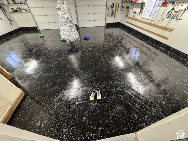 Garage featuring a high-gloss speckled epoxy floor coating, integrated wall-mounted storage tracks, and two overhead garage doors