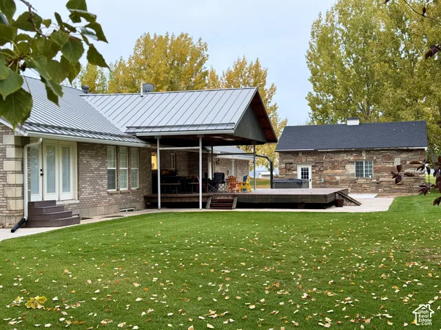 Brick exterior dwelling with a standing-seam metal roof, large covered deck, expansive lawn, and a separate stone-veneer structure
