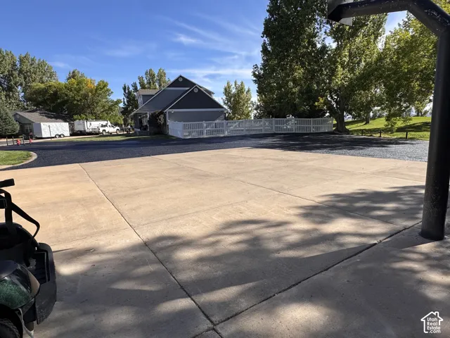 Expansive concrete driveway featuring paved transition to asphalt surfacing, perimeter white vinyl fencing, and mature trees