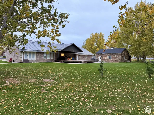 Expansive backyard featuring a brick exterior, standing-seam metal roof, covered patio, and detached stone-clad outbuilding