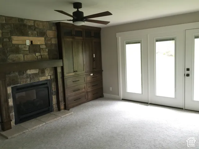 Stone fireplace with a prominent timber mantel, custom built-in wood cabinetry, ceiling fan, and double glass-paneled doors