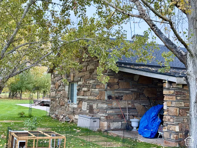 Detached garage featuring multi-tonal stone masonry, covered patio area, and mature trees on a landscaped lot