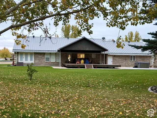 Exterior featuring a brick facade, standing seam metal roof, covered patio, attached deck, and built-in hot tub
