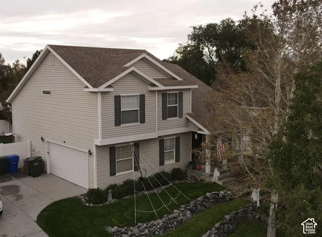 Two-story residence featuring horizontal siding, dark window shutters, an attached garage, concrete driveway, and rock-lined landscaping
