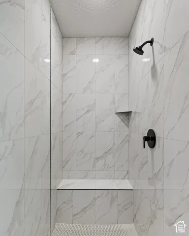 Walk-in shower featuring floor-to-ceiling large-format tile with a white and grey finish, matte black fixtures, integrated tile bench, and mosaic tile flooring