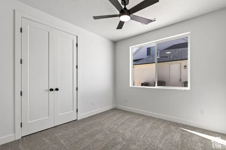 Neutral-toned carpeted room featuring double doors with matte black hardware, a multi-blade ceiling fan with an integrated light fixture, and a large horizontal sliding window