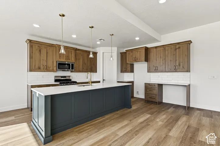 Kitchen featuring wood-finish cabinetry, a contrasting central island, white solid-surface countertops, subway tile backsplash, and recessed pendant lighting