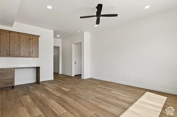 Wood-finish flooring, matte black ceiling fan, recessed lighting, and built-in cabinetry with white subway tile backsplash