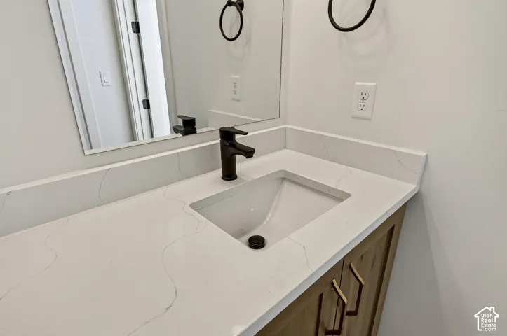 Vanity featuring a stone countertop, undermount sink, dark-finish hardware, wood-tone cabinetry, and a frameless mirror