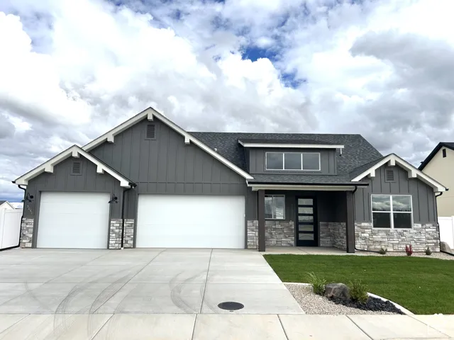 Exterior featuring vertical board-and-batten siding, stone veneer accents, multi-gabled roofline, three-car garage, and concrete driveway
