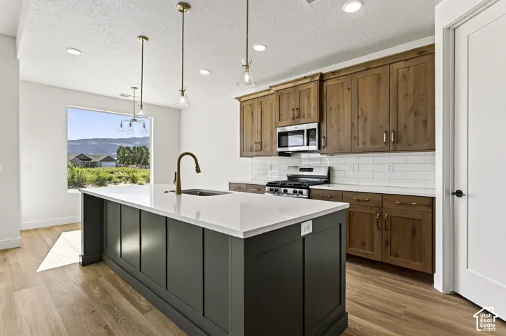 Kitchen featuring a center island with a stone-surface countertop, wood-finish cabinetry, white subway tile backsplash, stainless steel appliances, and wood-finish flooring