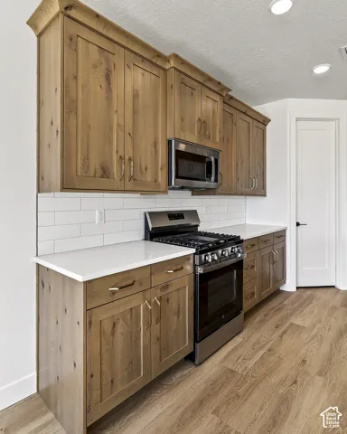 Kitchen featuring natural wood-finish cabinetry, solid-surface countertops, a white subway tile backsplash, stainless steel appliances, and wood-finish flooring