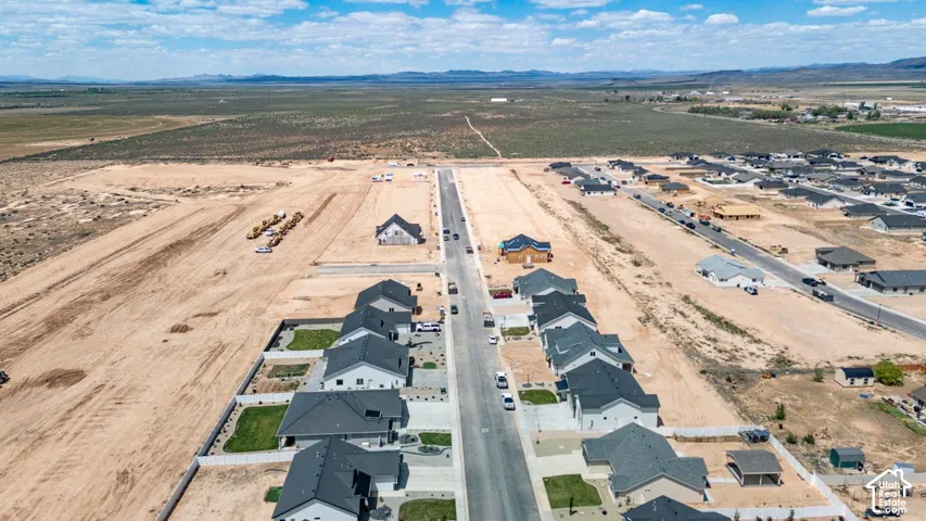 Aerial perspective of a residential development featuring asphalt streets, concrete sidewalks, and surrounding open landscape with distant mountain scenery