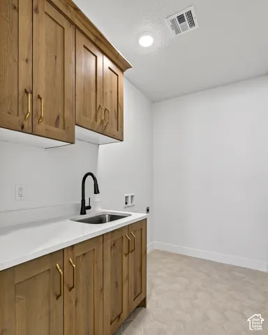 Custom wood-finish cabinetry with brass-tone hardware, white countertop, stainless steel undermount sink, matte black gooseneck faucet, and hexagonal tile flooring