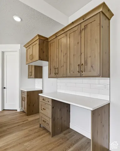 Custom cabinetry with stained wood finish, white subway tile backsplash, light-toned stone countertops, brass-toned hardware, and wood-finish flooring
