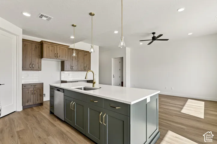 Kitchen featuring dark-toned cabinetry, a contrasting center island with a stone-finish countertop, stainless steel dishwasher, glass-shade pendant lighting, and wood-finish flooring