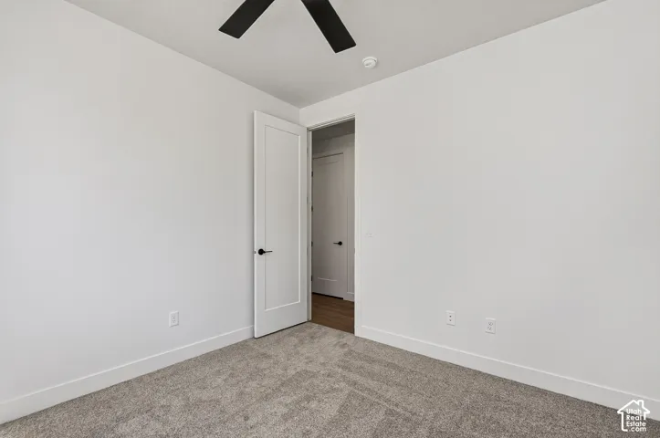 Neutral interior featuring wall-to-wall carpeting, crisp white walls, a matte black ceiling fan, and solid-core interior doors with matte black hardware