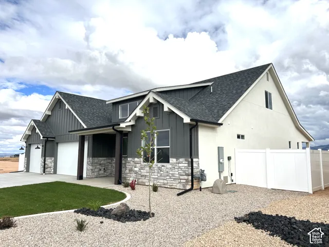 Exterior featuring board-and-batten siding, stone veneer masonry, multi-gabled roofline, concrete driveway, and white vinyl privacy fencing