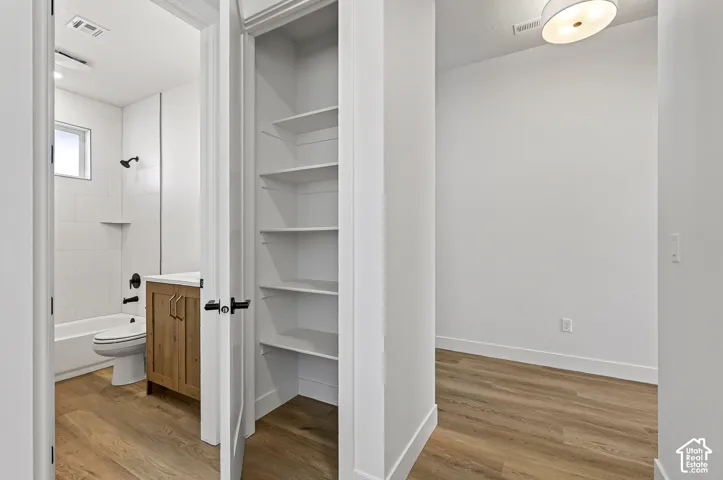 Bathroom featuring wood-finish flooring, a vanity with neutral-tone cabinetry, matte black plumbing fixtures, and a white tiled shower surround