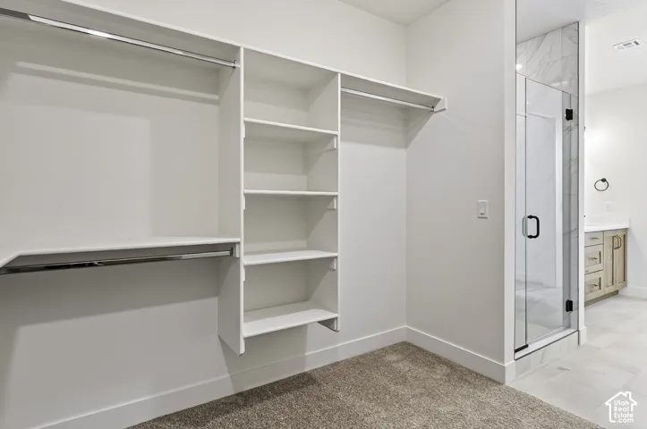 Walk-in closet featuring white built-in shelving and dual hanging rods, alongside a glass-enclosed shower with tiled surround and a vanity cabinet