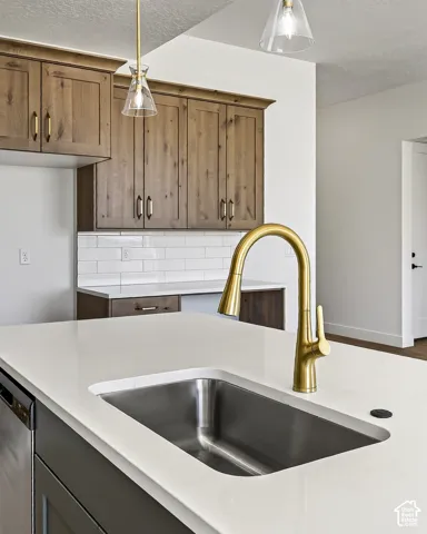Kitchen featuring a quartz-topped island with an undermount stainless steel sink, brass-finish pull-down faucet, white subway tile backsplash, and wood-finish cabinetry with brass-finish hardware