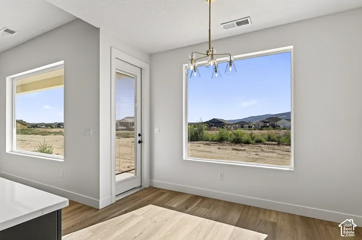 Neutral-toned interior featuring wood-finish flooring, oversized windows, an exterior glass-panel door, and a multi-arm modern chandelier
