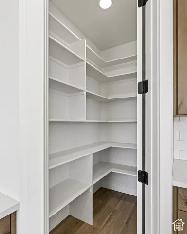 Walk-in storage featuring multi-level white shelving and wood-finish flooring