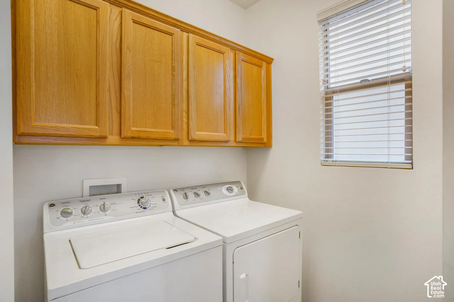 Laundry area featuring wood-finish wall-mounted cabinetry and a window with horizontal blinds
