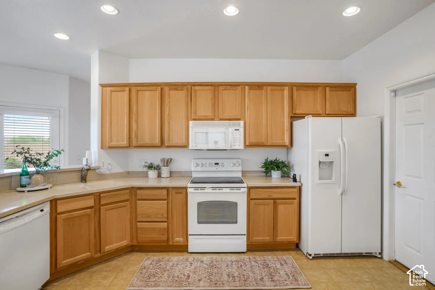 Kitchen featuring light wood-finish cabinetry, solid-surface countertops, recessed ceiling lighting, and white appliances