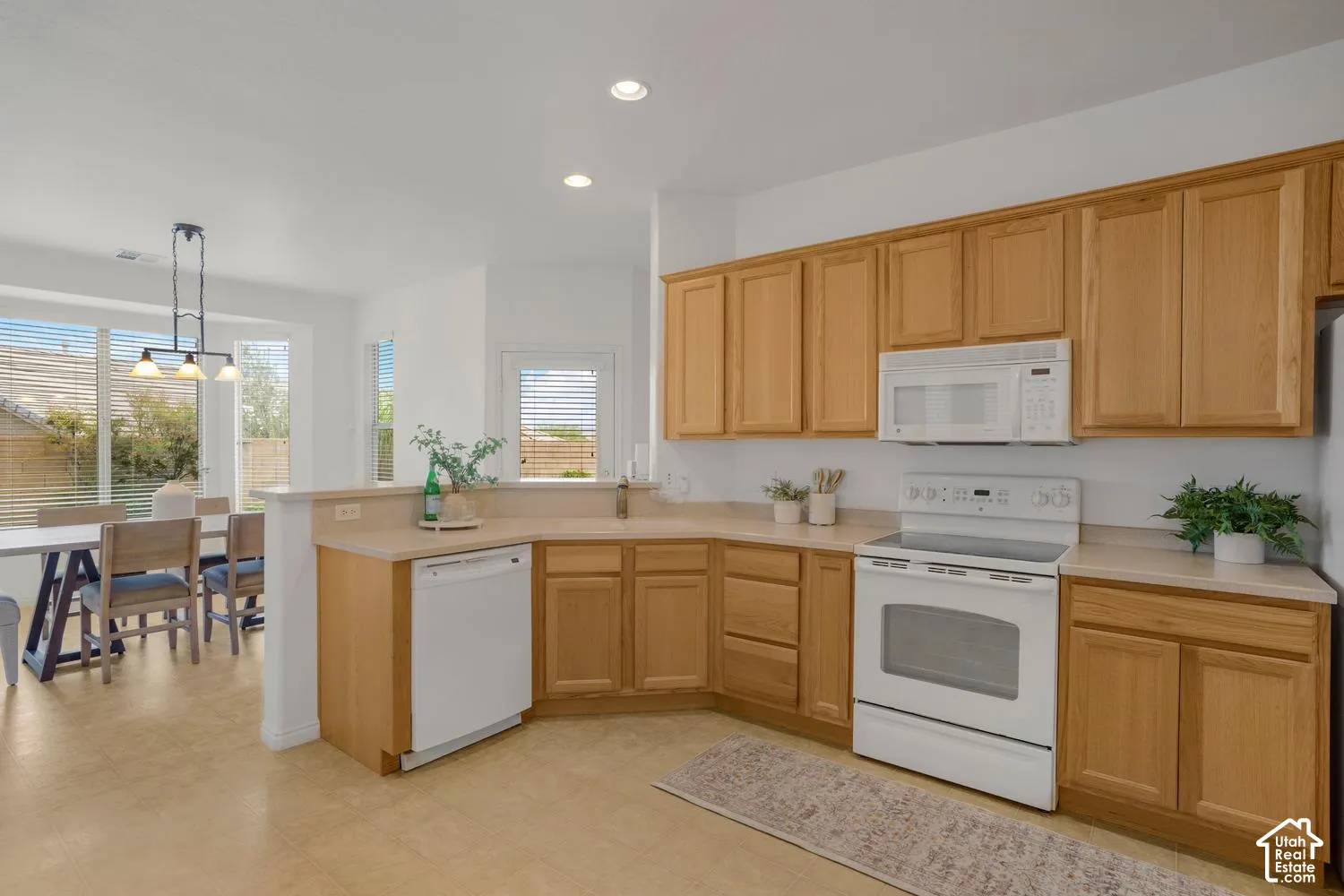 Kitchen featuring natural wood cabinetry, white appliances, integrated peninsula, and tiled flooring