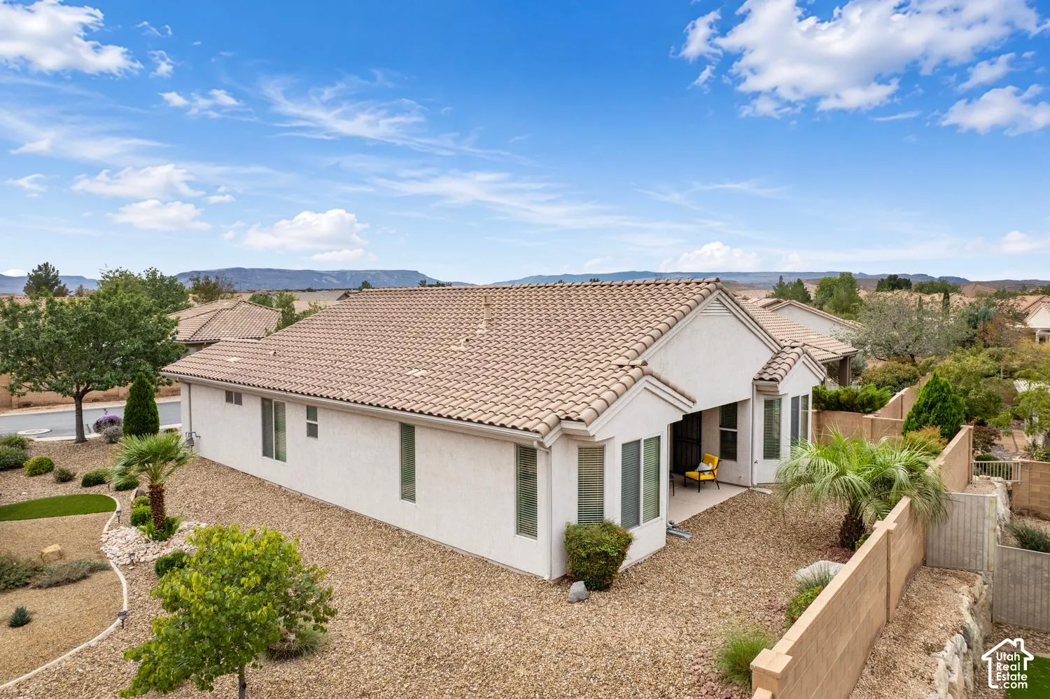 Stucco exterior with a tiled roof, covered patio, xeriscaped grounds, and perimeter fencing