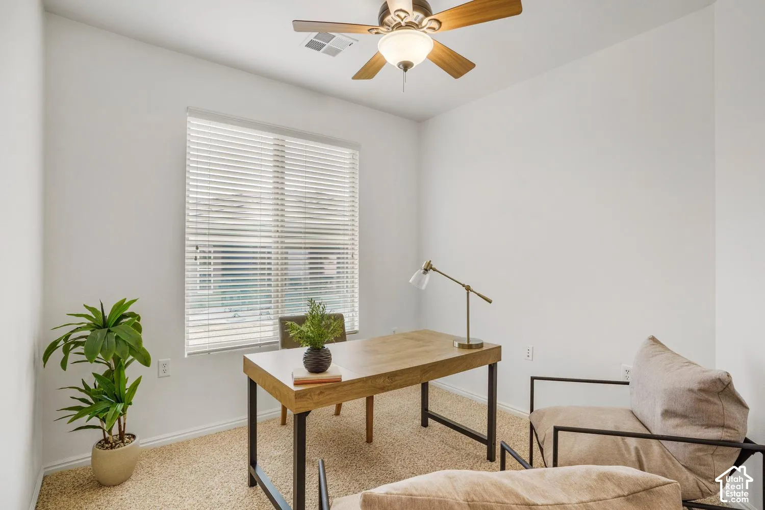 Neutral-toned interior room featuring wall-to-wall carpeting, a multi-blade ceiling fan with integrated lighting, and a large window fitted with horizontal blinds
