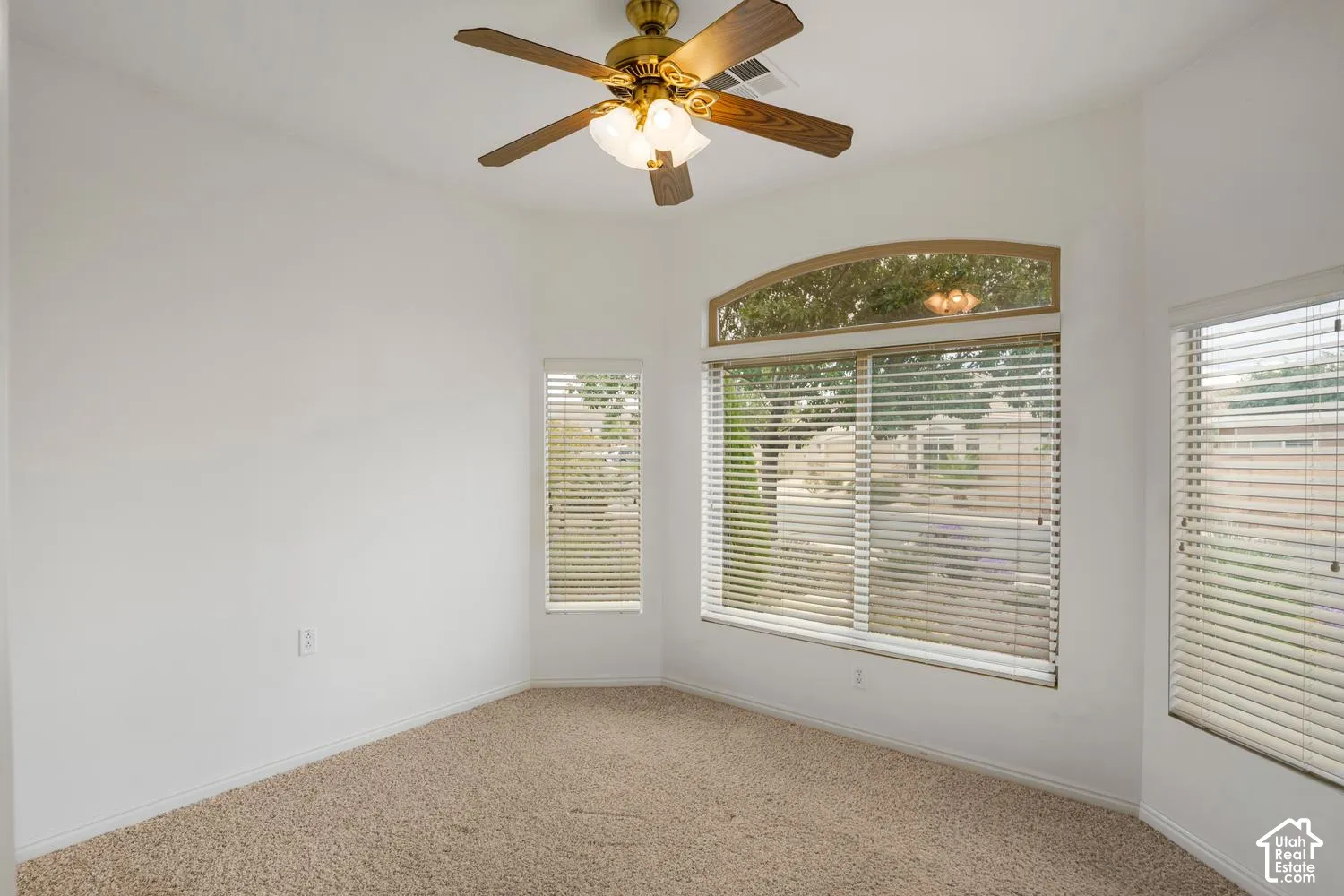 Textured wall-to-wall carpeting, ceiling fan with integrated lighting, and multiple windows including an arched transom window