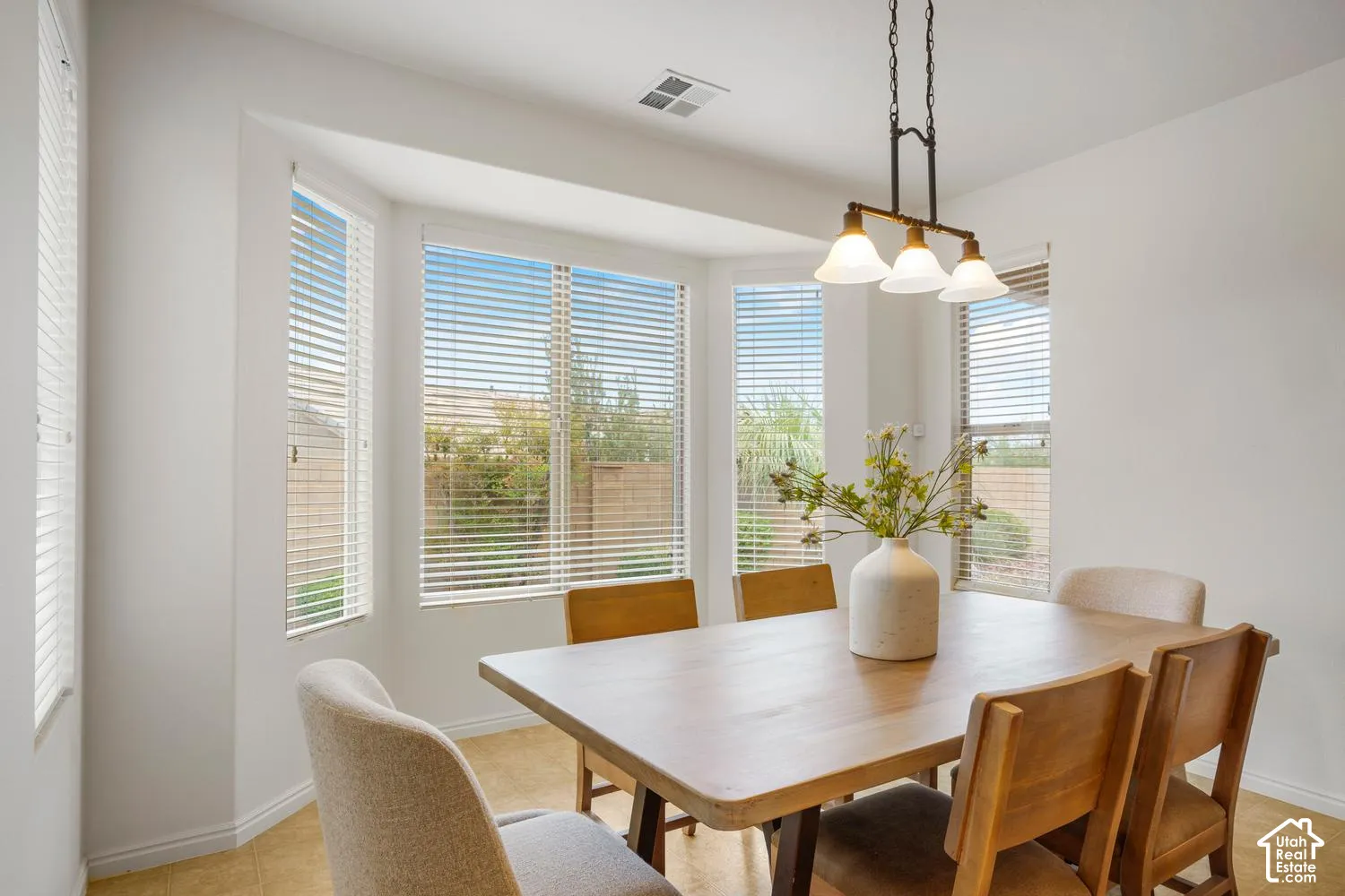 Bay window featuring multi-pane glass windows with horizontal blinds, neutral floor tile, and a three-light pendant fixture