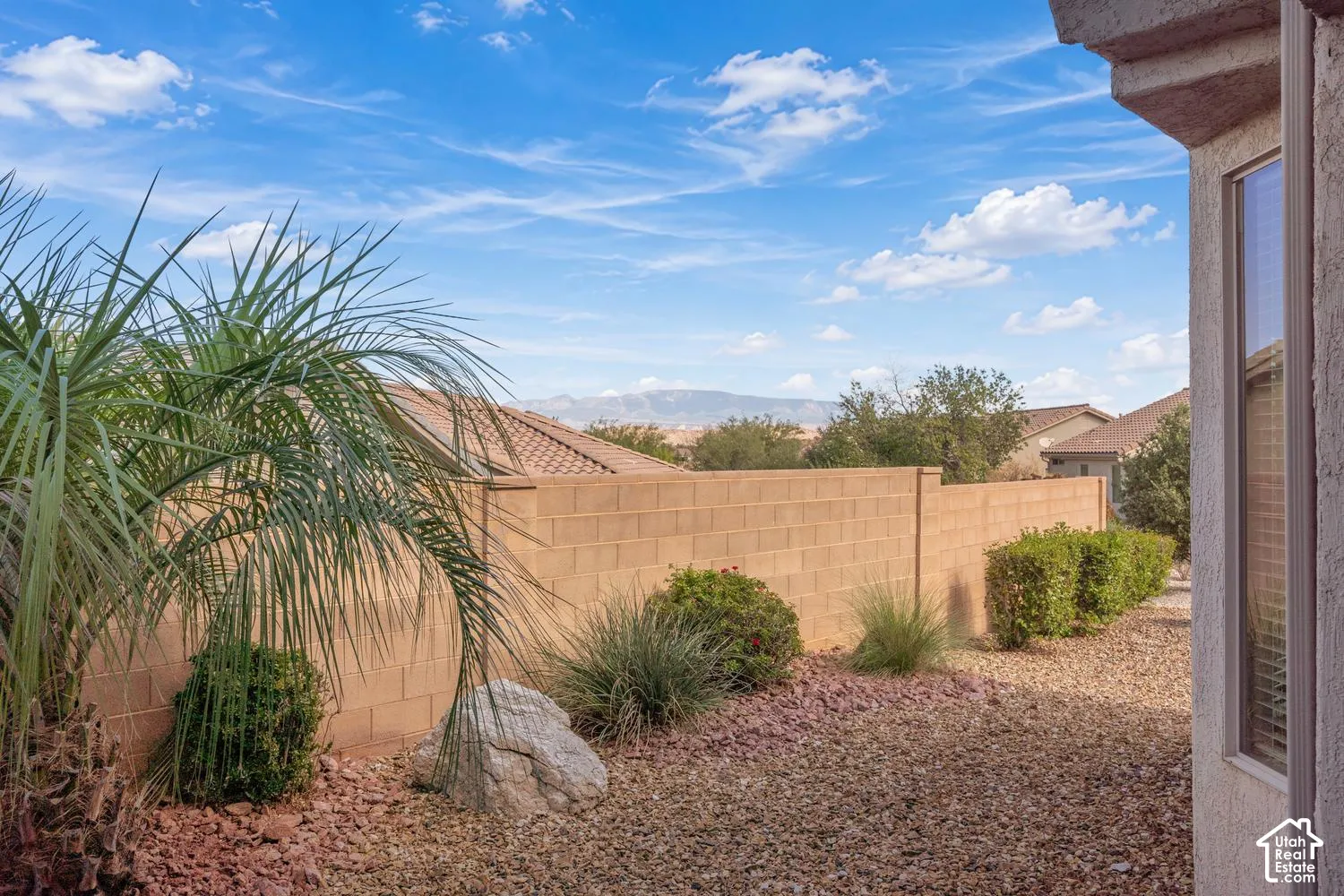 Landscaped exterior featuring a masonry block wall, rock ground cover, ornamental shrubs, and mountain scenery