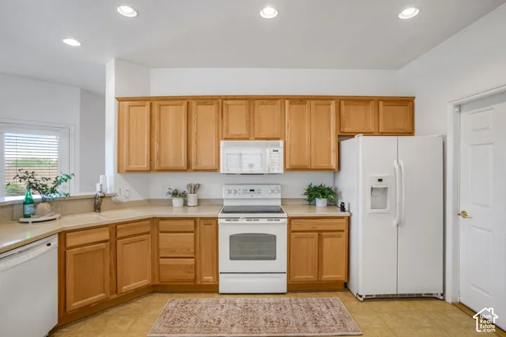 Kitchen featuring light wood-finish cabinetry, solid-surface countertops, recessed ceiling lighting, and white appliances