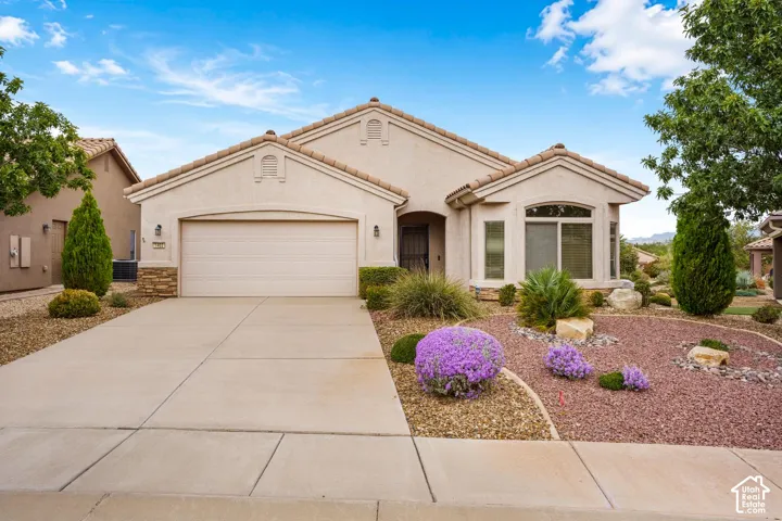 Single-story exterior featuring a neutral stucco facade, tile roofing, stone veneer accents, multi-pane bay windows, and an expansive concrete driveway