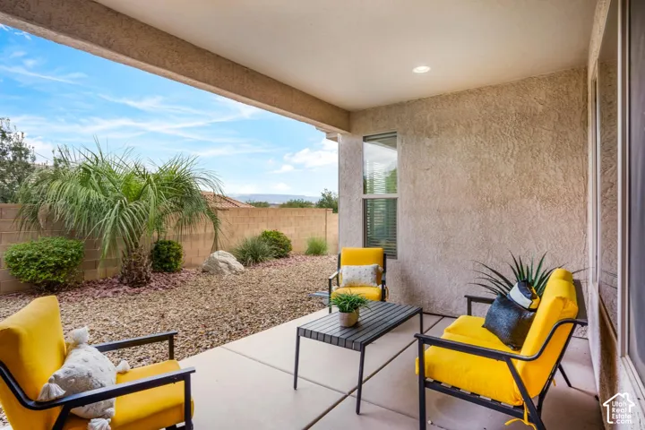 Covered concrete patio featuring recessed lighting, stucco exterior walls, and low-maintenance desert landscaping with decorative gravel and mature shrubbery enclosed by a masonry perimeter wall